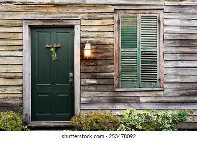 Old Rustic Vintage Dilapidated Antique House Home Building Structure With Green Intricate Front Door And Window With Shutters Closed And Porch Light Lantern Glowing Turned On