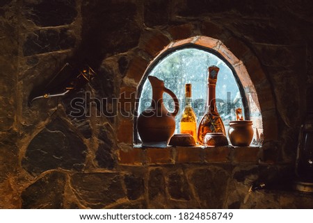 Old rustic wine bottles, jugs on a small cellar window on a stone wall Vintage winery home cellar Ceramic clay terracotta jug, pot, vase, kitchen souvenirs on shelf