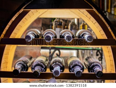 Old rustic wine rack with vine bottles illuminated house display of bottles in wooden stand made of old barrel 