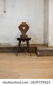 an old rustic wooden chair against a grungy and dirty white wall in an abandoned building
