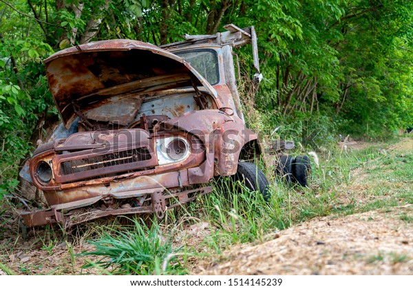 Old rusty abandoned car in the\
woods  after war.Abandoned vehicle dumped in countryside field.\
tree is growing out of the hood of an old classic car in a\
field