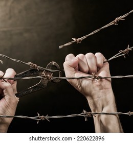 old rusty barbed wire with hand on the dark background - Shutterstock ID 220622896