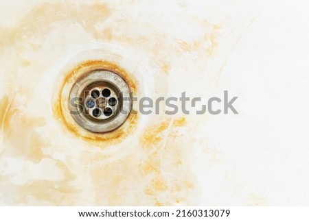 An old rusty bathtub surface with a metal drain hole. Dirty cracked unclean bath or sink with red rust stain, close-up. Corrosion, unsanitary concept, copy space.