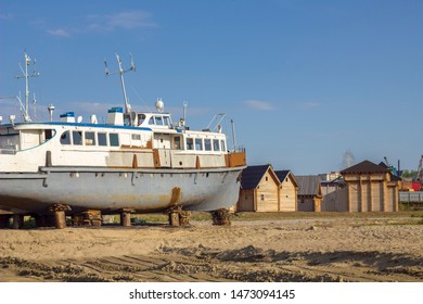 old rusty battered ship on supports on the shore against the background of wooden houses