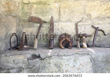 Old rusty blacksmith tools on the stone . The exhibition of blacksmith craft work examples on the wall in Local Ethnological Museum.