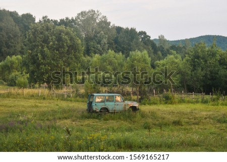 Old and rusty blue car abandoned at the edge of the forest. Dramatic scene with vintage damaged car left on the field.