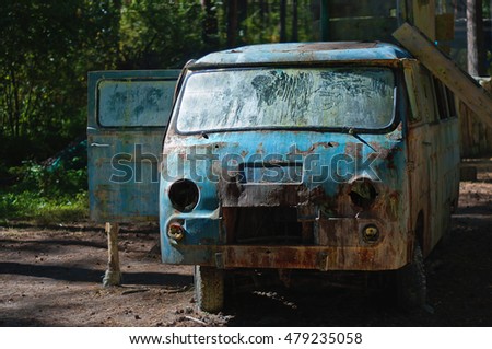 Old rusty broken minibus with paint marks after paintball fights. A paintball playground in the pine forest