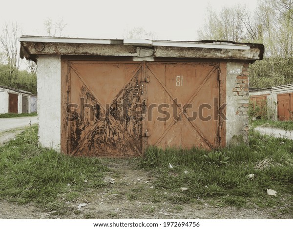 An old rusty\
brown metal car garage door with a padlock on the white brick wall.\
In the foreground - green\
grass.