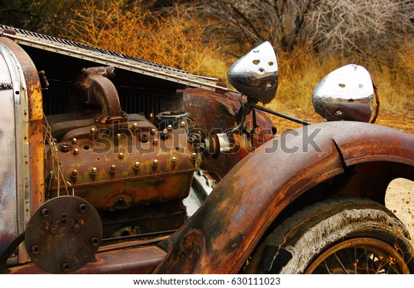 An old rusty car lies abandoned in the desert.\
Detail of the engine.