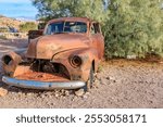 An old, rusty car is sitting in a desert. The car is in a junkyard and has been there for a long time. The car is covered in rust and has a lot of damage. The scene is desolate and abandoned