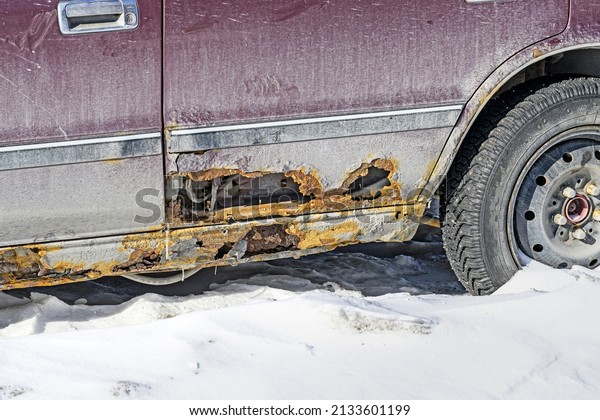 An\
old rusty car in a snowy parking lot on a sunny\
day