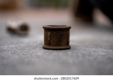 Old rusty cast iron pipe coupling sleeve standing on a textured concrete surface, representing obsolete plumbing parts, corrosion, and metal scrap hardware.