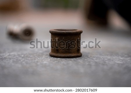 Old rusty cast iron pipe coupling sleeve standing on a textured concrete surface, representing obsolete plumbing parts, corrosion, and metal scrap hardware.
