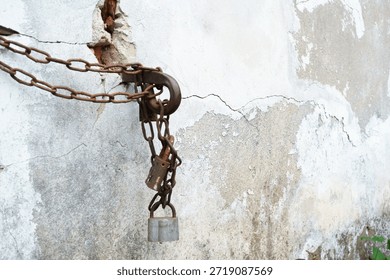 Old rusty chains and padlocks secured to a weathered, cracked concrete wall. Concept of industrial decay, urban security, and abandonment.