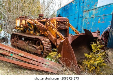 An Old Rusty Circa 1960's Bulldozer With Caterpillar Tracks Overgrown With Trees In An Auto Wrecker Scrap Yard