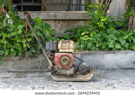 Old and rusty construction compactor machine left on broken concrete path near green plants in outdoor setting