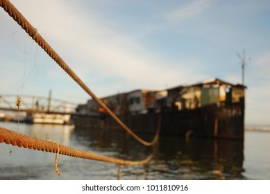 An Old Rusty Craft Stranded With A Thick Steel Cable To The Shore Of The Danube, On A Blue Sky Clear Weather.