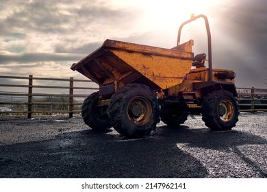 Old rusty dumper track parked on a parking lot in a country side. The vehicle is yellow color has many scratches. Warm sunny day. Dramatic sky. Construction and repair equipment for rent concept.