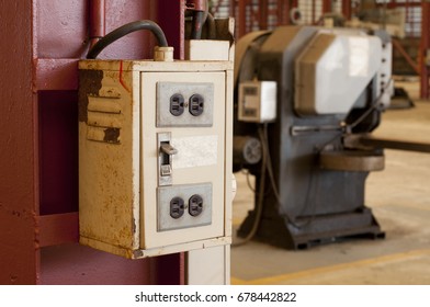 Old and rusty electrical box hanging on iron pillar in front of machine in factory
