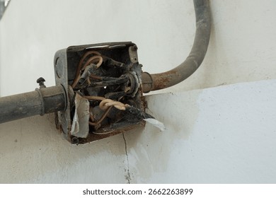 Old rusty electrical junction box on a concrete wall, The box is open and has several exposed electrical wires and several conduits running into the box.