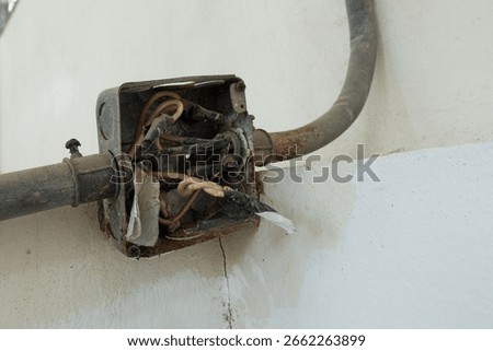 Old rusty electrical junction box on a concrete wall, The box is open and has several exposed electrical wires and several conduits running into the box.