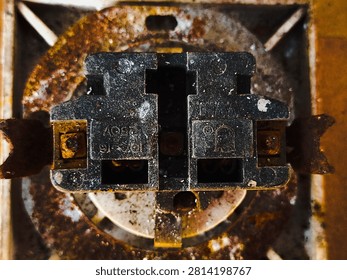 Old rusty electrical socket mechanism close up. Vintage dirty power outlet internal parts with heavy corrosion.
Macro photograph of the inside components of an antique wall power outlet. The black plastic body and surrounding metal ring show severe rust stains, oxidation, and grime buildup. Perfect for industrial grunge themes, hazardous electrical wiring concepts, vintage hardware, or texture backgrounds. Taken In Dau, Malang, East Java Indonesia, On July 19 2026