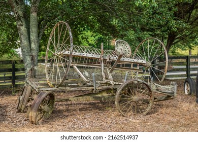 Old Rusty Horse-drawn Hay Rake Farm Equipment On Top Of A Broken Vintage Wagon Abandoned On A Farm Outdoors On A Sunny Day