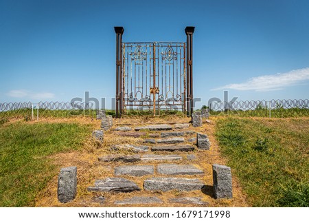 Old rusty iron gate in the middle of a field leading to nowhere. Concept of purgatory, limits, frontiers and freedom