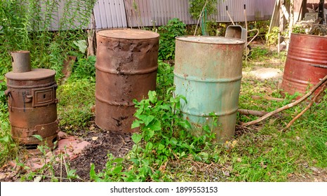 Old rusty metal barrels and a stove in the backyard of a rural house close-up on the grass for scrap metal and for incineration of garbage disposal.