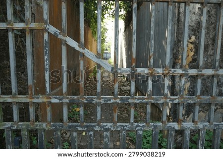 Old rusty metal gate blocking a narrow abandoned alley between weathered concrete walls