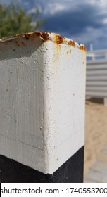 Old Rusty Metal Pillar Painted In White And Black Colors. White Painted Metallic Surface With Rusty Drips And Stains Closeup