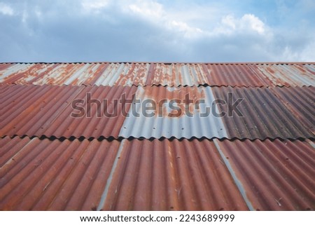 old rusty metal roof with cloudy blue sky as background, barn warehouse roof