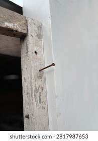 Old rusty nail driven into a weathered white wooden door frame, close-up details.