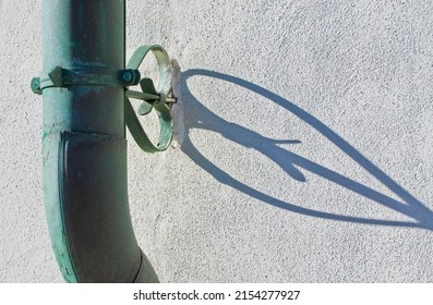 Old rusty oxidized copper downpipe against a plaster wall with shadow