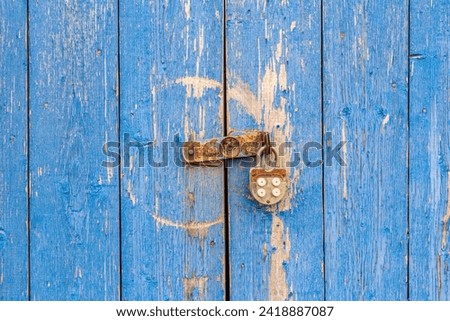 An old rusty padlock on an old wooden door with weathered blue paint