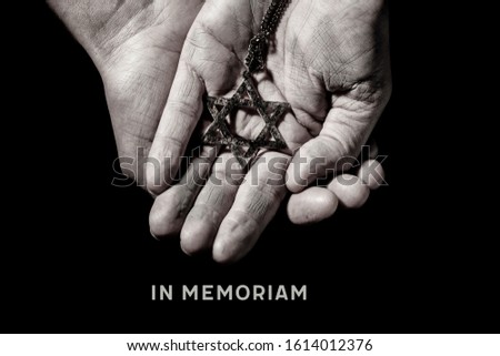 an old and rusty pendant in the shape of the star of david on the hands of a man and the text in memoriam, a latin phrase equivalent to in memory, as a memory of the dead jewish people