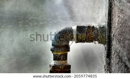 Old rusty pipe with leak and water spraying out under pressure leaky leaking