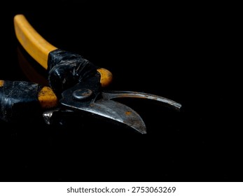 Old rusty pruning shears with yellow handles on a reflective dark surface