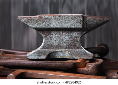 Old rusty rugged anvil on top of other blacksmith tools on black wooden background.
