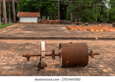 Old rusty soil compactor abandoned on a brick yard, surrounded by clay roof tiles and trees, showing obsolete rural technology replaced by modern agriculture.