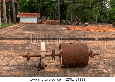 Old rusty soil compactor abandoned on a brick yard, surrounded by clay roof tiles and trees, showing obsolete rural technology replaced by modern agriculture.