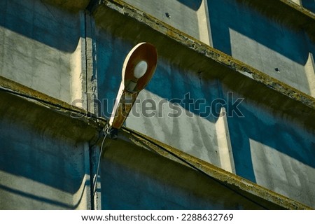 An old, rusty street lighting lantern hangs on the concrete wall of an old warehouse, a colorful street scene