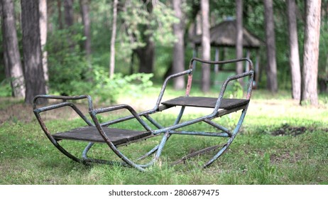 Old rusty swing gently sways in a peaceful forest clearing. Vintage abandoned playground bench rocking softly among trees on a sunny summer day