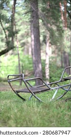 Old rusty swing gently sways in a peaceful forest clearing. Vintage abandoned playground bench rocking softly among trees on a sunny summer day