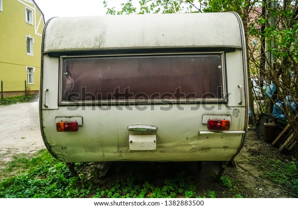 old rusty travel trailer (camper\
trailer, camper van, caravan). Side view.Caravan Trailer Near\
house. Summer Holidays Road Trip Travel Concept.emblem of\
berlin