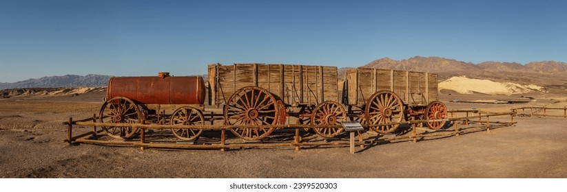 Old rusty unused historic Twenty Mule Teams vehicle of three vagoons with water reservoir in desert of Death Valley national park in america with blue sky at sunny day, usa