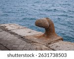 Old, rusty and worn bollard on the dock. Sea in the background.