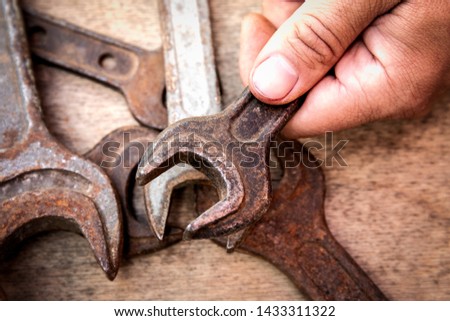 Old and rusty wrench in hand on wooden background.  Construction and hand tools, maintenance and reparing concept