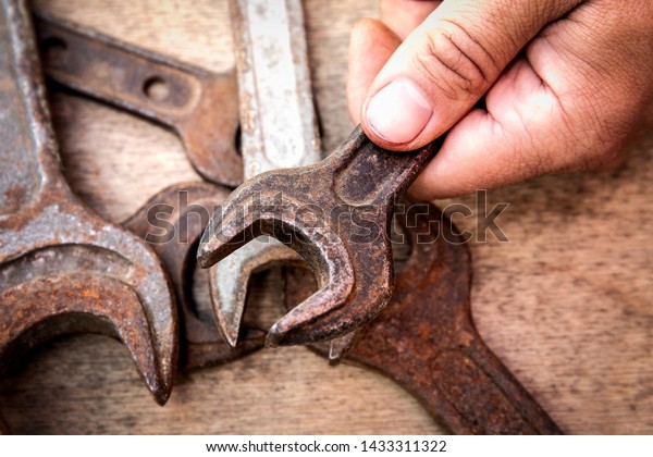 Old and\
rusty wrench in hand on wooden background.  Construction and hand\
tools, maintenance and reparing\
concept