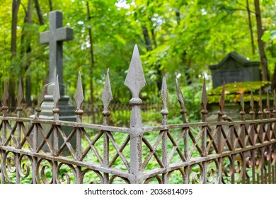 An old rusty wrought-iron cemetery fence on an overgrown grave with a cross and a crypt. Lutheran cemetery in St. Petersburg, Russia